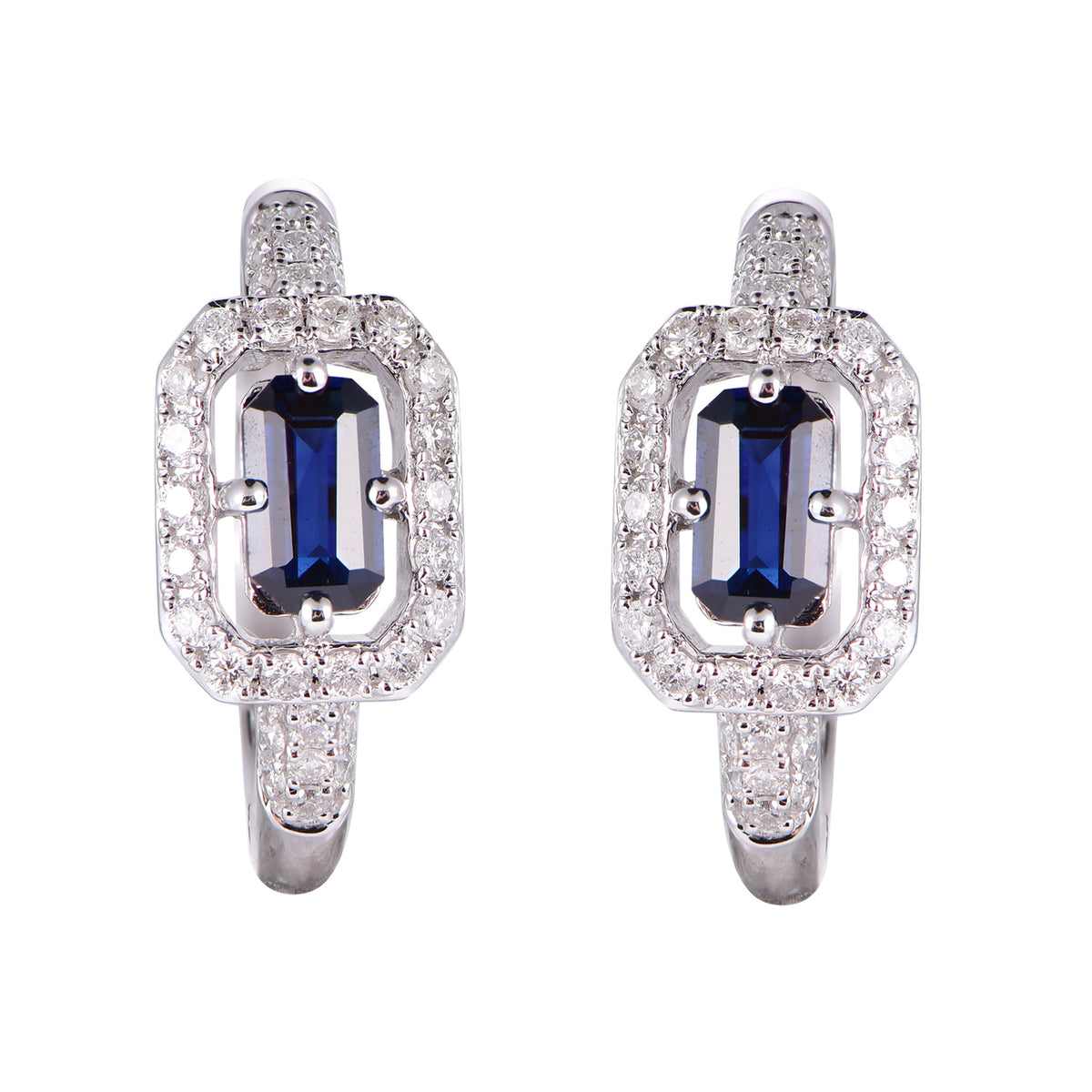 A pair of silver-toned huggie earrings featuring a central baguette-cut blue sapphire surrounded by a halo of small clear stones, set against a plain white background.